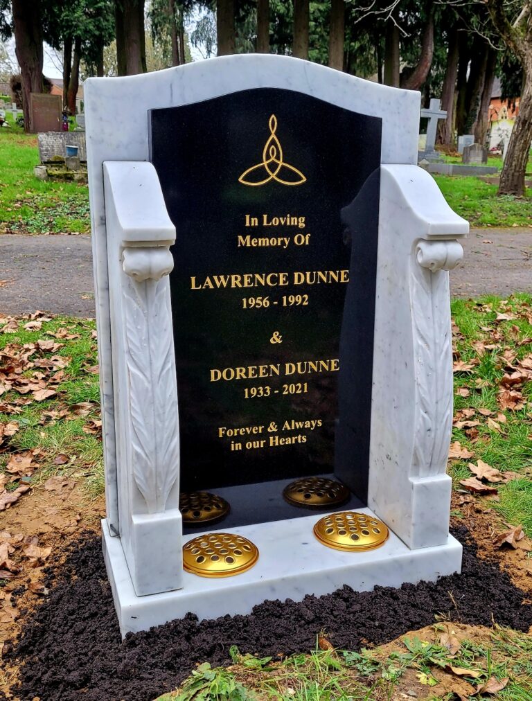 Black granite headstone in a white marble surround with gold lettering
