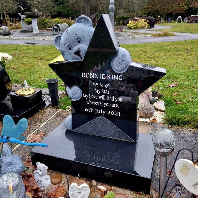 Black granite star-shaped child's memorial with gold lettering and a teddy bear